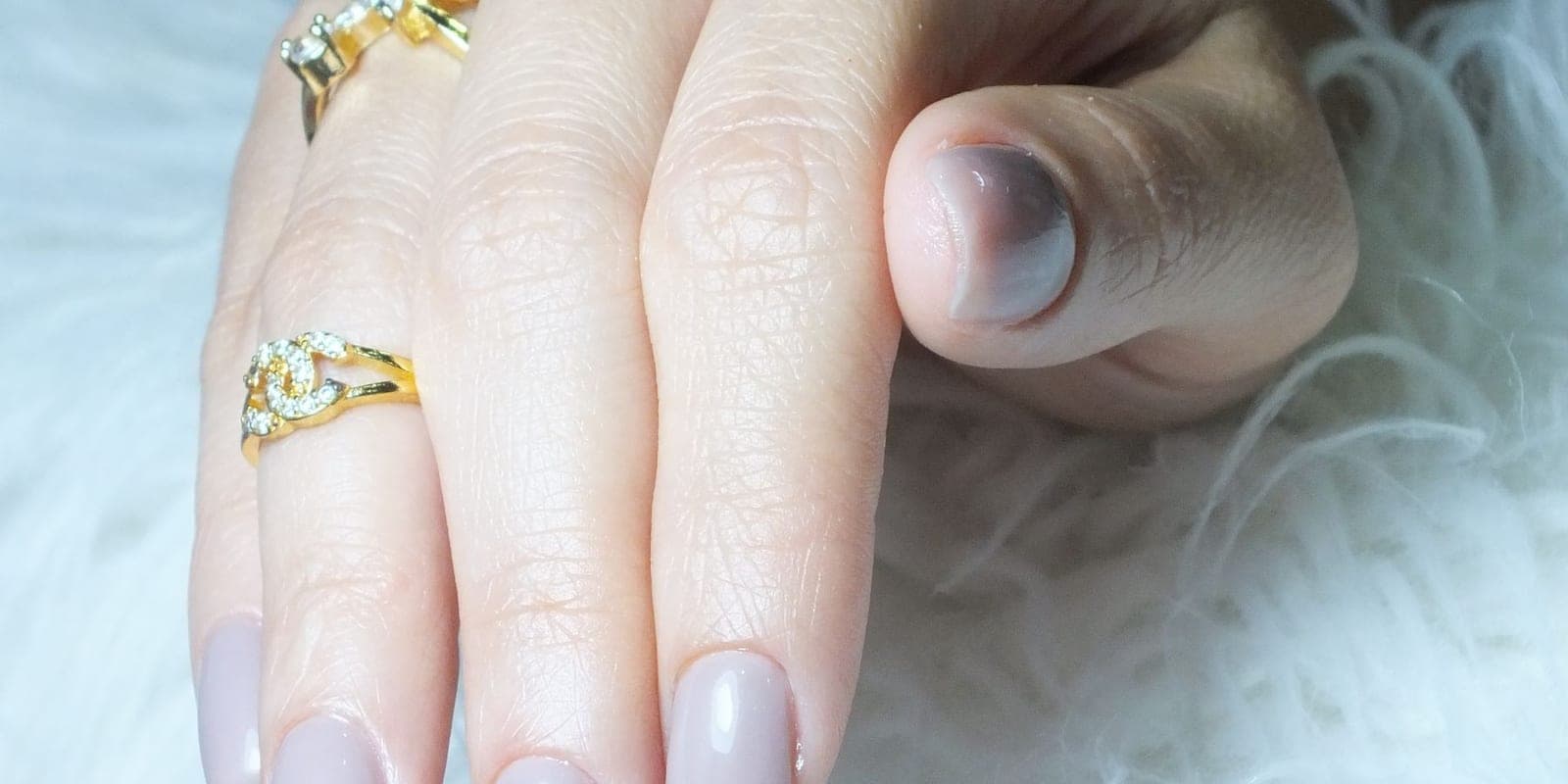 Elegant manicured hand wearing stacked gold rings, lit softly