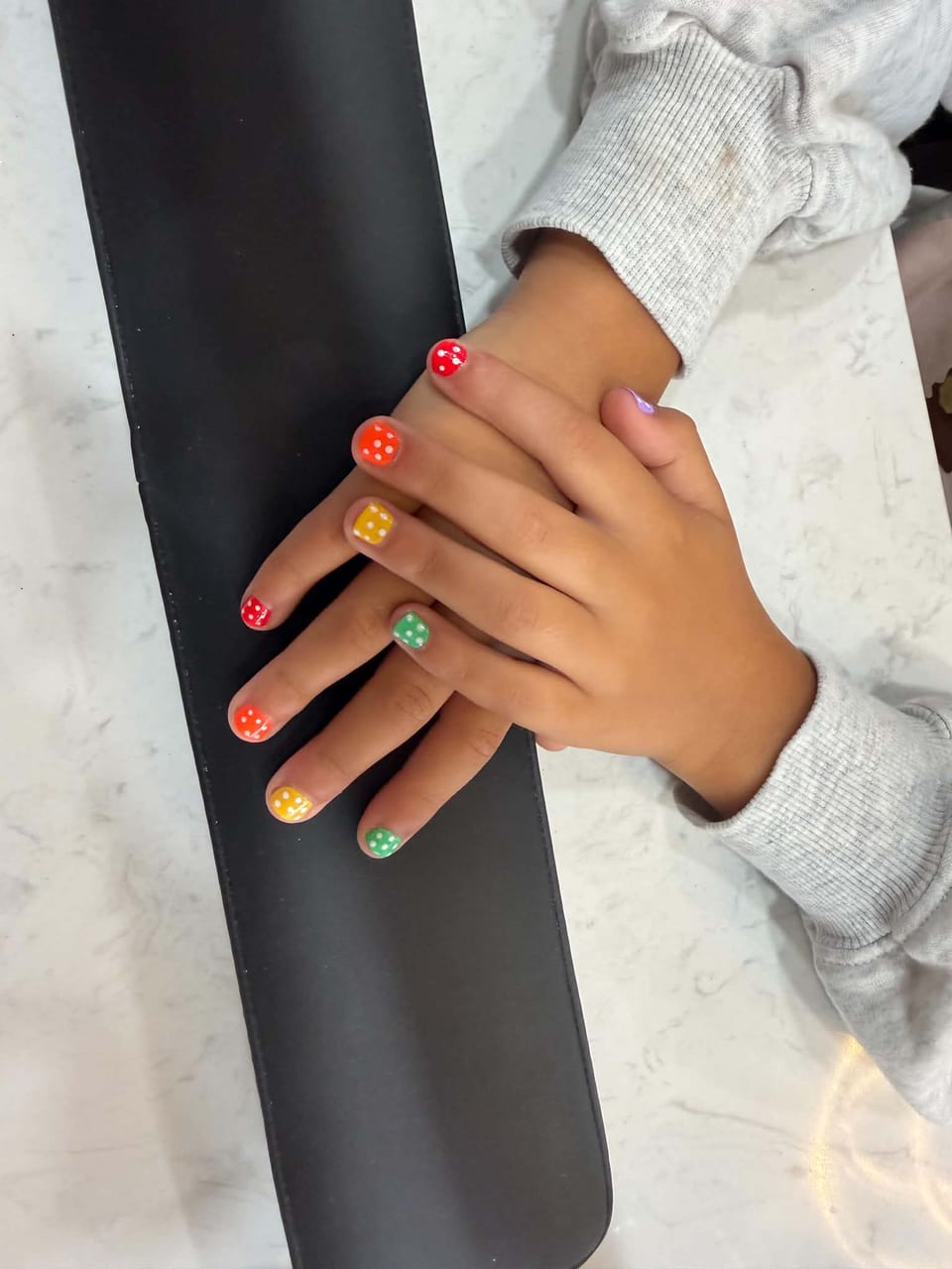 A child’s manicure in red, orange, yellow and green with white polka dots